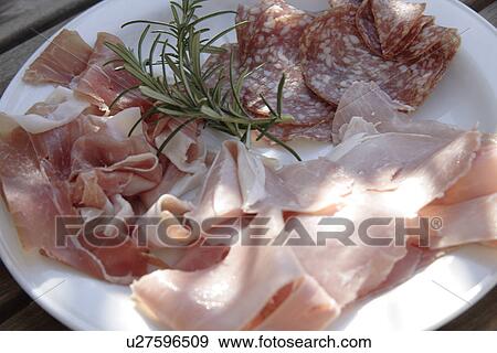 Stock Photo - Plate of cold cuts: raw and cooked ham, salami, rosemary, close up. Fotosearch