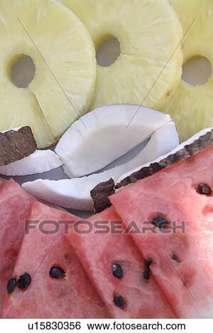 Stock Photograph - Tropical fruit prepared on plate: pineapple, watermelon, coconut, overhead view. Fotosearch