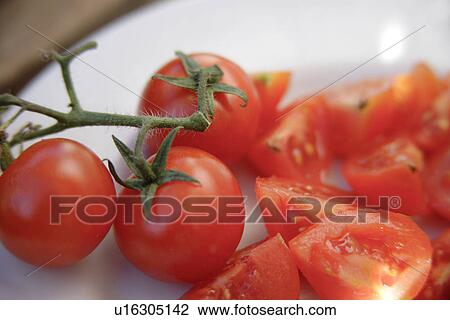 Stock Image - Whole and quarters of tomato on white plate, close up. Fotosearch