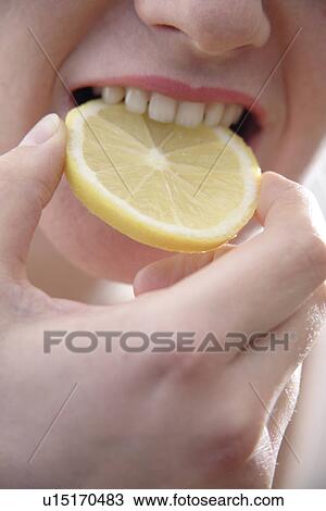 Stock Image - Woman biting in slice of lemon, close up. Fotosearch