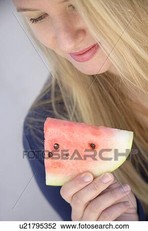 Stock Image - Young blond woman eating a slice of watermelon, close up. Fotosearch