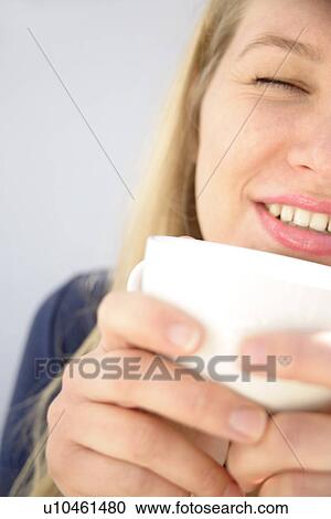 Stock Image - Young blond woman holding cup of tea, close up. Fotosearch