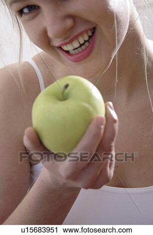 Stock Image - Young blond woman holding green apple, close up. Fotosearch