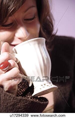 Stock Photo - Young brunette woman holding cup of coffee, close up. Fotosearch