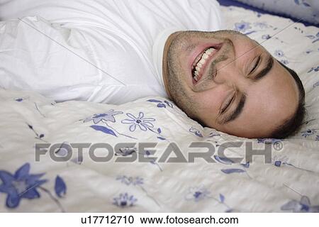 Young man lying in bed, smiling and relaxing View Large Photo Image Stock Image - Young man lying in bed, smiling and relaxing. Fotosearch
