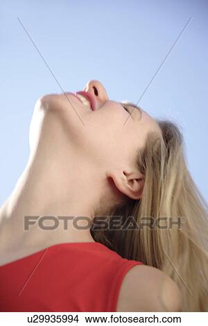 Picture - Young woman in a happy mood in front of blue sky, view from below. Fotosearch