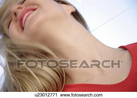 Stock Image - Young woman tossing her long blond hair in front of blue sky, view from below. Fotosearch