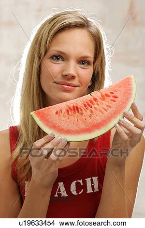 Picture - Young woman with long blond hair eating a slice of watermelon, portrait. Fotosearch