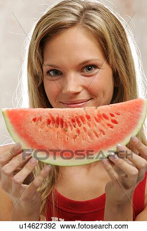 Stock Image - Young woman with long blond hair eating a slice of watermelon, portrait. Fotosearch