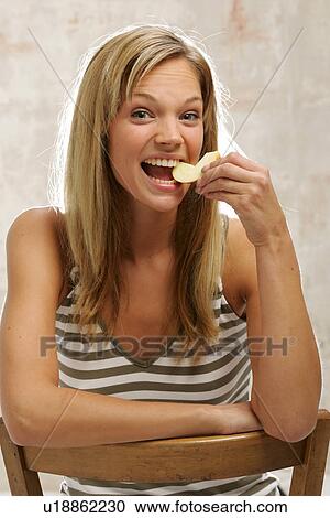 Stock Image - Young woman with long blond hair eating an apple, portrait. Fotosearch