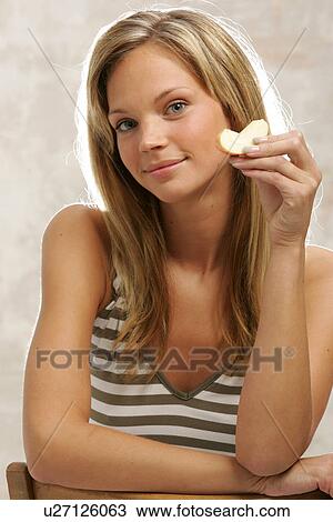 Stock Image - Young woman with long blond hair eating an apple, portrait. Fotosearch