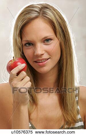 Stock Photography - Young woman with long blond hair eating an apple, portrait. Fotosearch