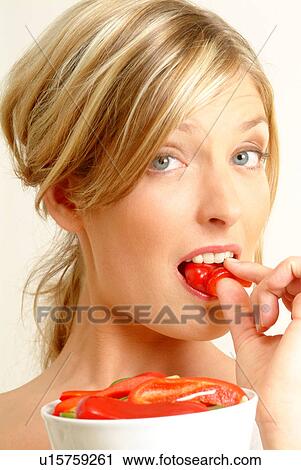 Stock Image - Portrait of woman eating red pepper. Fotosearch