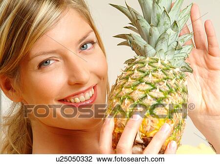 Stock Image - Portrait of woman holding pineapple. Fotosearch