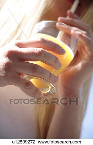 Stock Image - Woman drinking orange juice with straw from glass, close up. Fotosearch