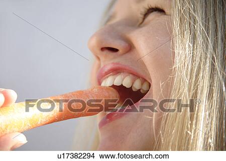 Young blond woman biting in fresh carrot, side view, close up View Large Photo Image Picture - Young blond woman biting in fresh carrot, side view, close up. Fotosearch
