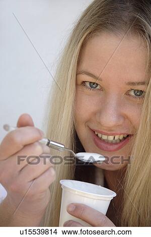 Picture - Young blond woman eating pure yogurt, close up. Fotosearch