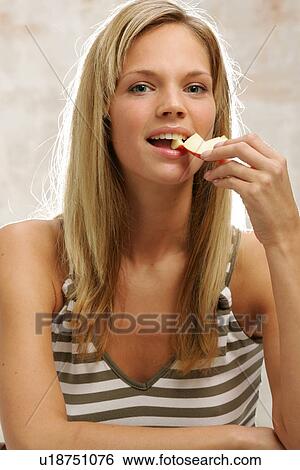 Stock Photograph - Young woman with long blond hair eating an apple, portrait. Fotosearch