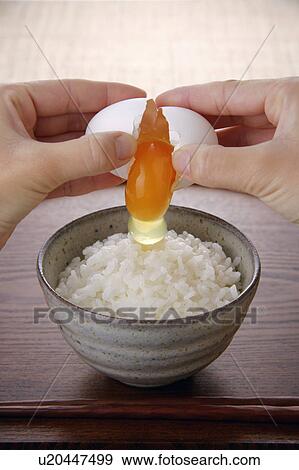 Stock Photo - A woman cracking an egg above steamed rice. Fotosearch