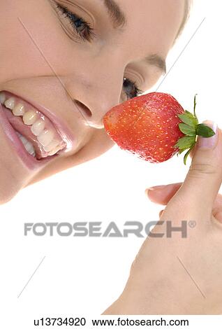 Stock Image - Close-up of a young woman holding a strawberry and grining. Fotosearch