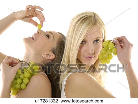 Stock Image - Close-up of two young women holding bunches of grapes. Fotosearch