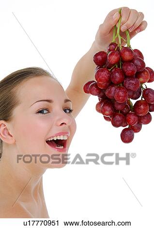 Stock Image - Portrait of a young woman holding a bunch of red grapes. Fotosearch
