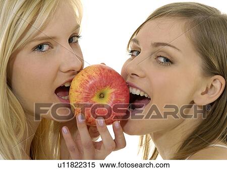 Stock Photography - Portrait of two young women eating an apple. Fotosearch
