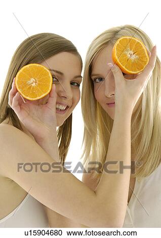 Stock Image - Portrait of two young women holding cross sections of a orange. Fotosearch