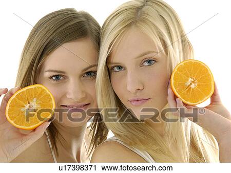 Stock Image - Portrait of two young women holding cross sections of a orange. Fotosearch