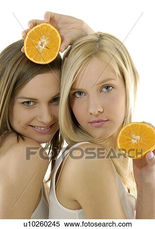 Stock Photography - Portrait of two young women holding cross sections of a orange. Fotosearch