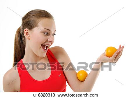 Stock Image - Close-up of a young woman balancing two oranges on her hand. Fotosearch