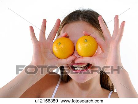 Stock Photo - Close-up of a young woman holding two oranges in front of her eyes. Fotosearch