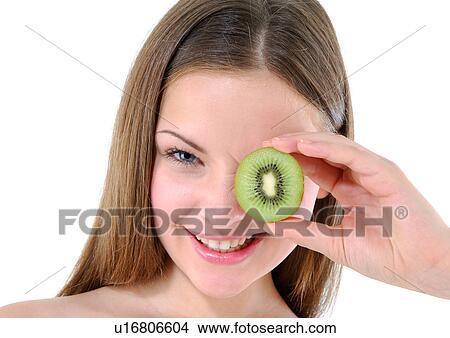 Portrait of a young woman holding a half kiwi fruit in front of her eye View Large Photo Image Picture - Portrait of a young woman holding a half kiwi fruit in front of her eye. Fotosearch