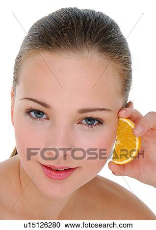 Stock Image - Portrait of a young woman holding a slice of orange. Fotosearch