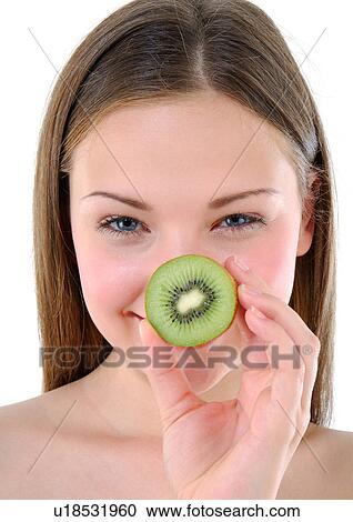 Stock Image - Portrait of a young woman holding a half kiwi fruit in front of her nose. Fotosearch