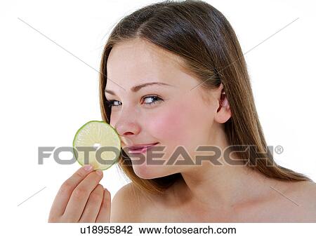 Stock Image - Portrait of a young woman holding a slice of a lime. Fotosearch