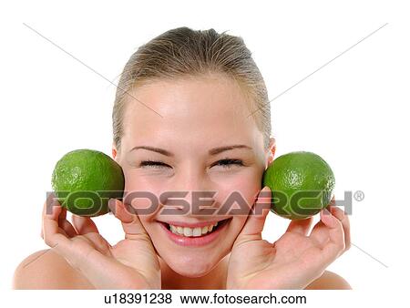 Portrait of a young woman holding two limes besides her two cheek and smiling View Large Photo Image Stock Photo - Portrait of a young woman holding two limes besides her two cheek and smiling. Fotosearch