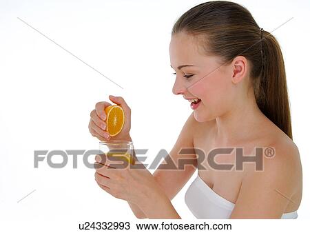 Stock Image - Side profile of a young woman squeezing an orange. Fotosearch