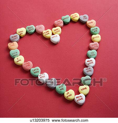Stock Photography - Colorful candy hearts with sayings on them arranged in shape of heart on red background.. Fotosearch