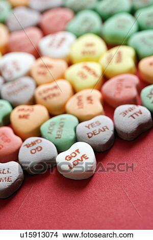 Picture - Group of colorful candy hearts with sayings on them arranged on red background.. Fotosearch