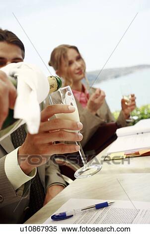 Stock Photography - Man and woman at table with others being served champagne. Fotosearch
