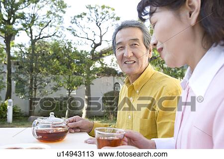 Stock Image - A Senior Adult Couple Having a Tea Break in a Garden, Side View. Fotosearch