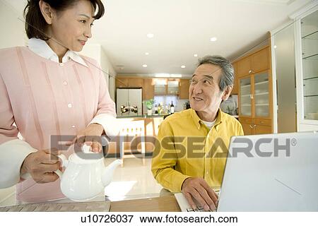 Stock Photo - A Senior Adult Couple Relaxing in a Dining Room, Front View. Fotosearch