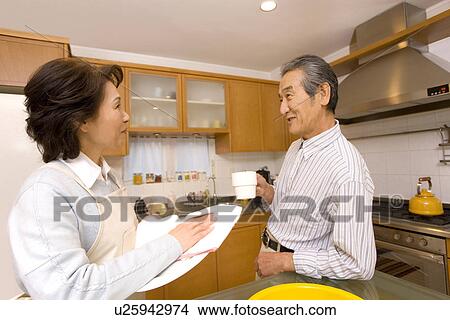 Picture - A Senior Adult Couple Talking in a Kitchen, Side View. Fotosearch