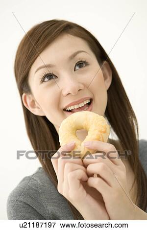 Stock Photo - A woman smiling and holding a doughnut, front view, white background. Fotosearch