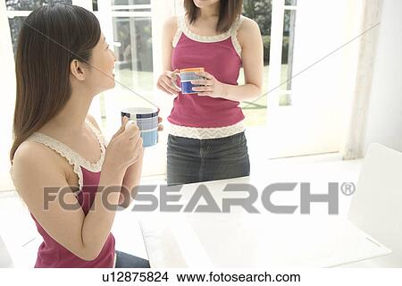 Picture - Two Women Wearing the Same Clothes, Standing and Sitting on a Chair . Fotosearch