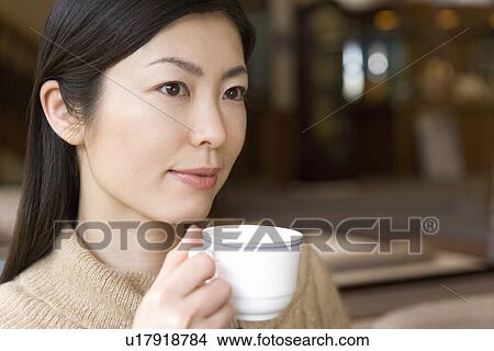 Woman sitting and holding a cup in the lobby, front view, Japan View Large Photo Image Picture - Woman sitting and holding a cup in the lobby, front view, Japan. Fotosearch
