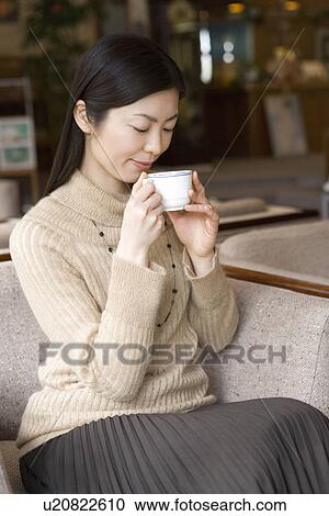 Stock Image - Woman sitting and holding a cup in the lobby, side view, Japan. Fotosearch