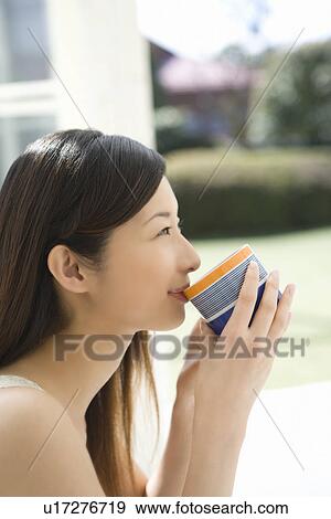 Stock Photo - Young Woman Drinking, Holding a Cup, Smiling, Side View. Fotosearch