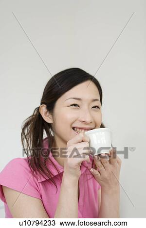 Stock Image -  Young Woman Holding a Cup, Smiling, Side View. Fotosearch